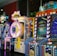 A row of brightly colored arcade game machines is arranged in a line against the wall. Each machine features vibrant lights and designs, with themes ranging from claw games to game show-inspired setups. The area has a playful and inviting atmosphere, suitable for entertainment or amusement centers.